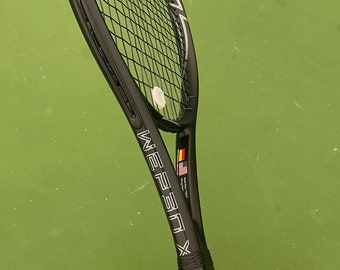 May include: A black tennis racket with white strings and the text "NEOSEN X" on the handle. The racket is on a green tennis court.