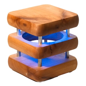 May include: A wooden lamp with a square base and three tiers. The lamp has a blue light that shines through the open spaces in the tiers.