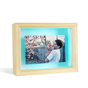 May include: A wooden picture frame with a light blue backlight, showcasing a photo of a father holding a young child in front of a flowering tree.