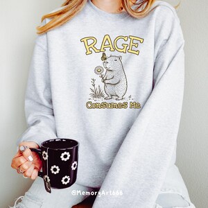 Funny capybara meme PNG SVG design featuring a cute vintage-style capybara holding a daisy flower with a butterfly resting on its head and bold retro “RAGE Consumes Me” typography. Funny sarcastic animal graphic with whimsical hand-drawn line art, soft neutral tones, and trendy unhinged aesthetic. Perfect for funny t-shirts, hoodies, mugs, tote bags, stickers, sublimation projects, Cricut SVG cut files, retro boutique apparel, instant digital download, 300 DPI transparent background.