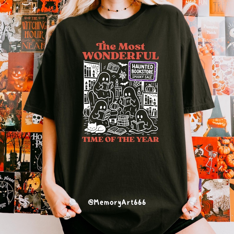 K&ouml;nnte beinhalten: Schwarzes T-Shirt mit einer wei&szlig;en Grafik, die Geister beim Lesen von B&uuml;chern, eine Katze und den Text "The Most Wonderful Time of the Year" zeigt. Das Design enth&auml;lt den Text "Haunted Bookstore Spooky Sale".