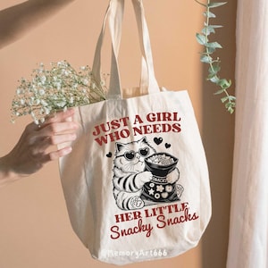 May include: A white canvas tote bag with the text "Just a girl who needs her little snacky snacks" in red. A cartoon cat wearing sunglasses holds a bag of snacks.