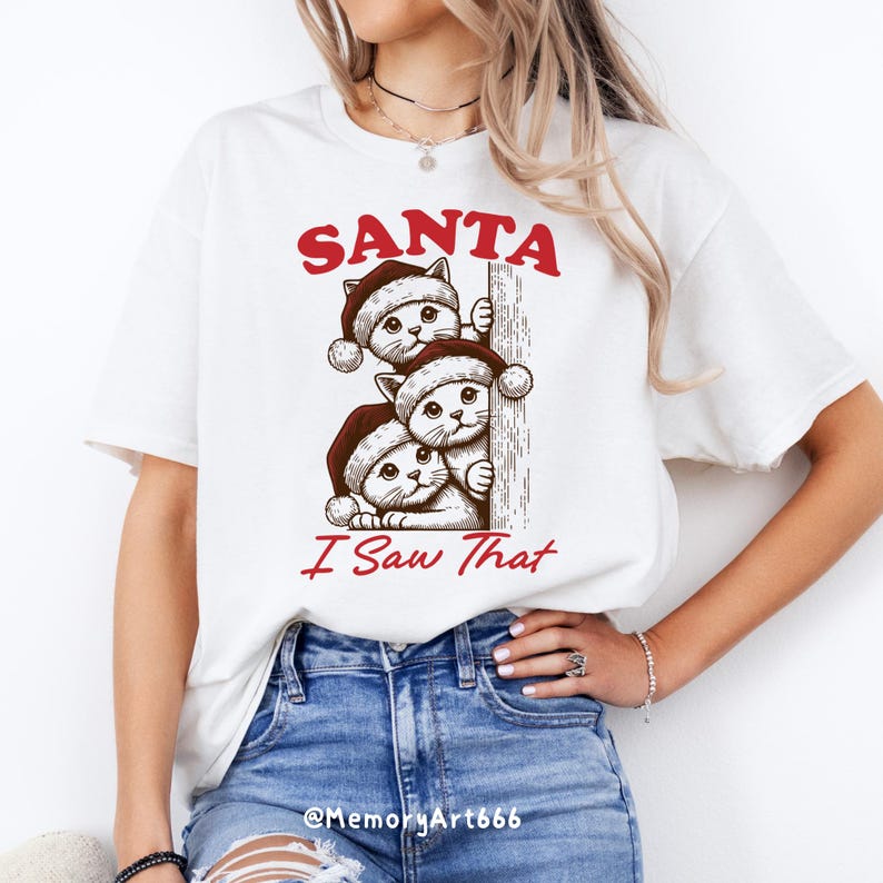 May include: White t-shirt featuring a red and black graphic of three cats wearing Santa hats peeking around a corner. The text "SANTA I Saw That" is printed below the cats.