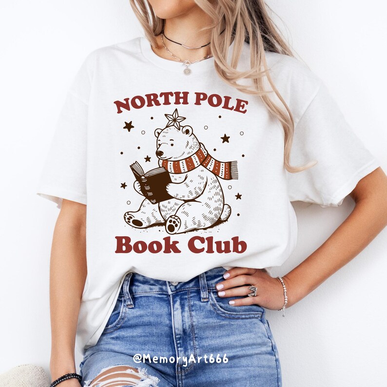 May include: White t-shirt with a brown illustration of a polar bear wearing a red and white scarf and reading a book. The text "North Pole Book Club" is printed in red on the shirt.