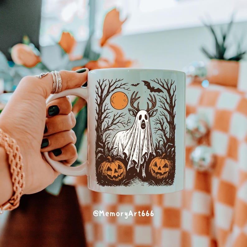 May include: White ceramic mug featuring a Halloween-themed design. The illustration includes a ghost with deer antlers, a full moon, bare trees, bats, and jack-o'-lanterns. The mug has a white handle and the text "@MemoryArt666" at the bottom.