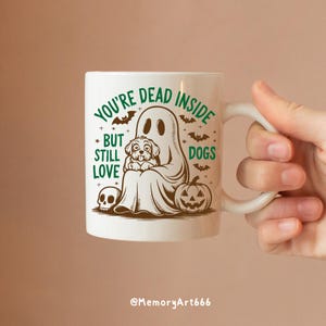 May include: White ceramic coffee mug with a green and brown illustration of a ghost holding a dog. The text on the mug reads "You're Dead Inside But Still Love Dogs".
