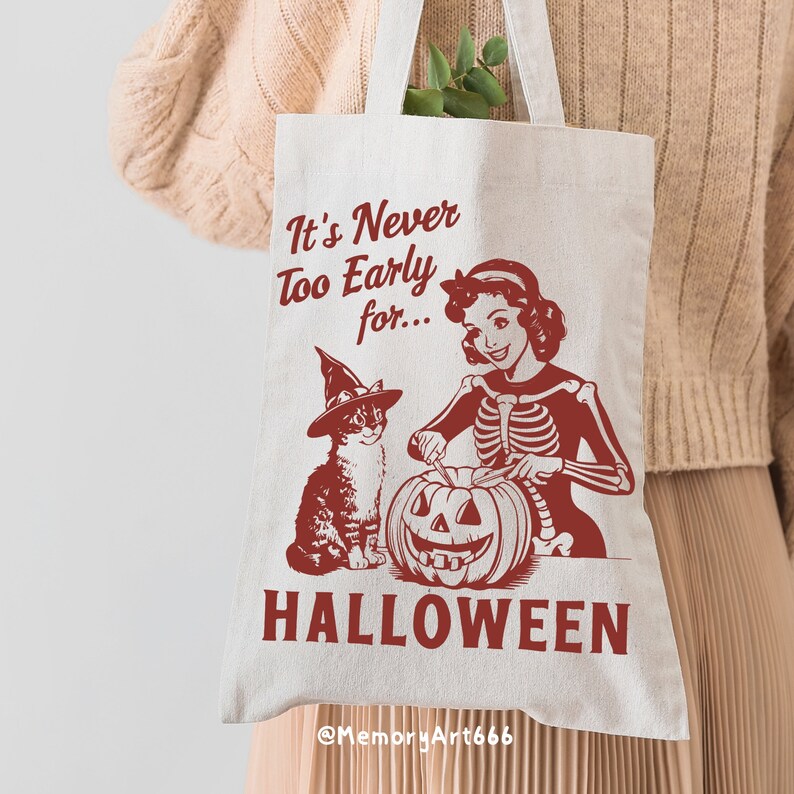 Puede incluir: Una bolsa de tela blanca con un gr&aacute;fico rojo de una mujer esqueleto tallando una calabaza con un gato que lleva un sombrero de bruja. El texto en la bolsa dice "It's Never Too Early for... HALLOWEEN @MemoryArt666"