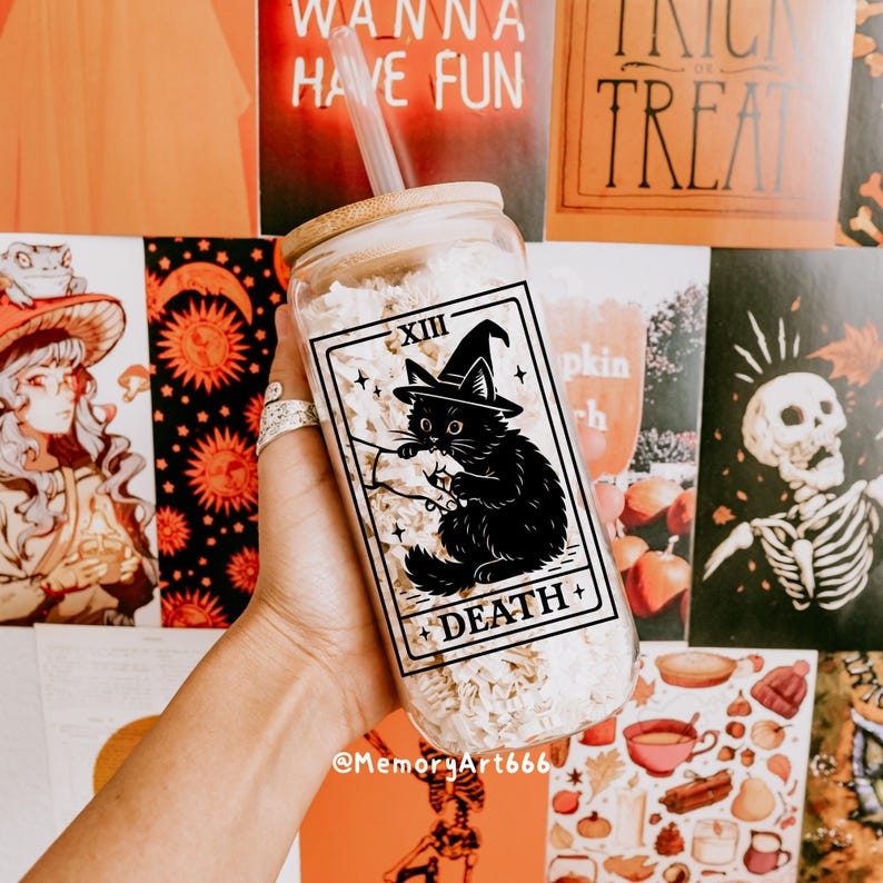 May include: A clear glass tumbler with a bamboo lid and straw. The tumbler features a black cat wearing a witch hat, with the text "DEATH" and "XIII" on the front. The tumbler is filled with a white substance.