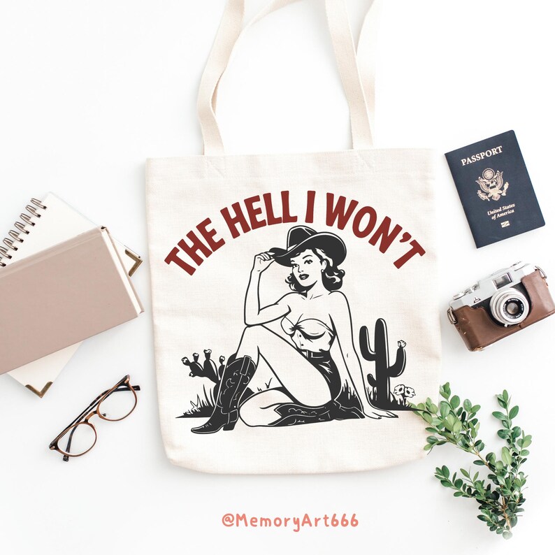 May include: A white canvas tote bag with a red and black graphic design. The graphic features a woman wearing a cowboy hat and boots, sitting with a cactus. The text "THE HELL I WON'T" is written in a circle around the woman. The text "@MemoryArt666" is printed at the bottom of the bag.