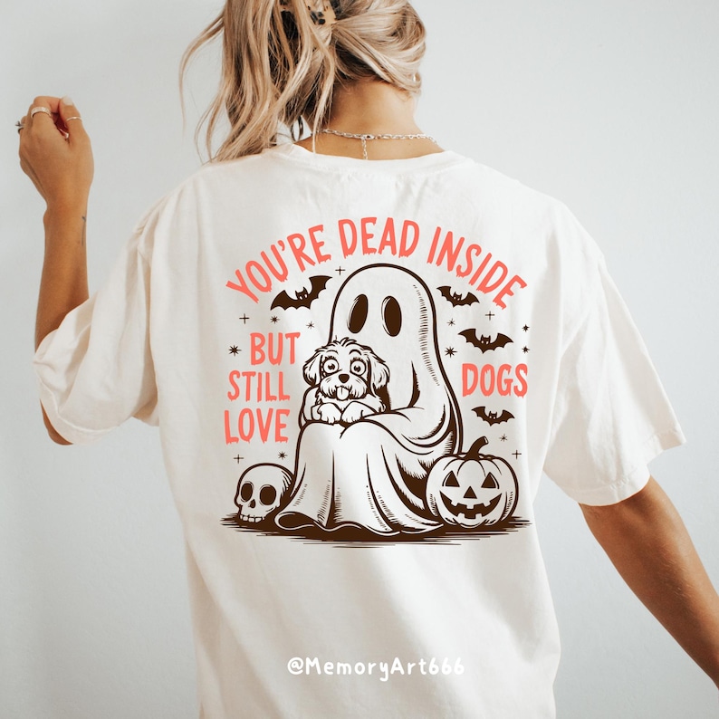 May include: White t-shirt with a graphic of a ghost holding a dog. The text on the shirt reads "You're Dead Inside But Still Love Dogs".