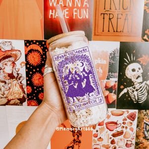 May include: A clear glass tumbler with a bamboo lid and straw. The tumbler features a purple graphic of three witches with the text "THE WITCH" and "VIII". The background includes Halloween-themed decorations.