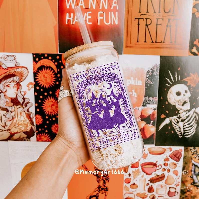 May include: A clear glass tumbler with a bamboo lid and straw. The tumbler features a purple graphic of three witches with the text "THE WITCH" and "VIII". The background includes Halloween-themed decorations.