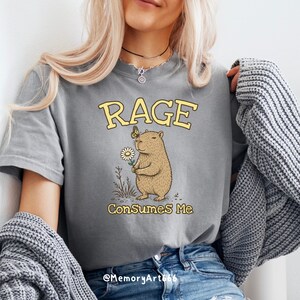 Funny capybara meme PNG SVG design featuring a cute vintage-style capybara holding a daisy flower with a butterfly resting on its head and bold retro “RAGE Consumes Me” typography. Funny sarcastic animal graphic with whimsical hand-drawn line art, soft neutral tones, and trendy unhinged aesthetic. Perfect for funny t-shirts, hoodies, mugs, tote bags, stickers, sublimation projects, Cricut SVG cut files, retro boutique apparel, instant digital download, 300 DPI transparent background.