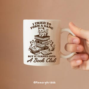 May include: White ceramic mug with a brown illustration of three cats reading books. The text on the mug reads "I tried to form a gang but it turned into a book club".