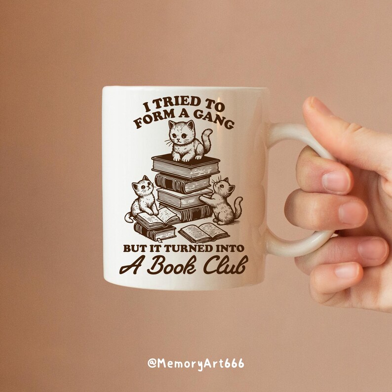 May include: White ceramic mug with a brown illustration of three cats reading books. The text on the mug reads "I tried to form a gang but it turned into a book club".