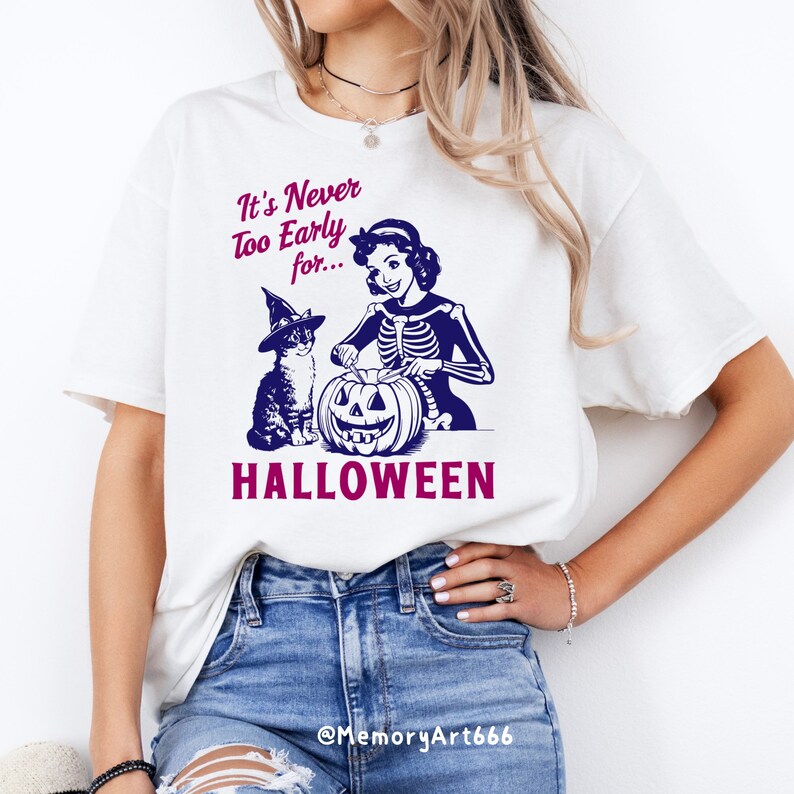 Puede incluir: Camiseta blanca con una ilustraci&oacute;n vintage de una mujer con un disfraz de esqueleto tallando una calabaza con un gato que lleva un sombrero de bruja. El texto en la camiseta dice "It's Never Too Early for... HALLOWEEN".