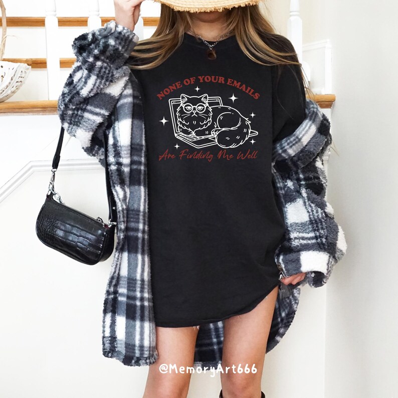 May include: Black t-shirt with a white illustration of a cat wearing glasses and sitting on a laptop. The text "None of your emails are finding me well" is written in red.