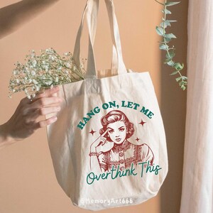 A vintage retro-style illustration of a 1950s woman with curled hair, resting her finger on her temple in a thoughtful pose. The text reads “HANG ON, LET ME” above and “Overthink This” below in playful retro typography. Monochrome hand-drawn line art with mid-century cartoon style and sparkle accents on a warm neutral background. Anxiety and mental health humor quote design, perfect for funny women’s shirts, mugs, tote bags, stickers, and digital crafts. Digital download SVG and PNG files.
