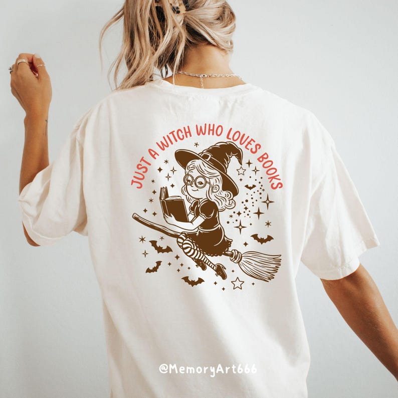 Może przedstawiać: Biały T-shirt z brązową ilustracją czarownicy czytającej książkę podczas lotu na miotle. Tekst "Just a witch who loves books" jest nadrukowany na koszulce na pomarańczowo.