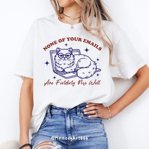 May include: White t-shirt with a blue and white illustration of a cat wearing glasses and sitting on a laptop. The text "NONE OF YOUR EMAILS ARE FINDING ME WELL" is printed in red on the shirt.