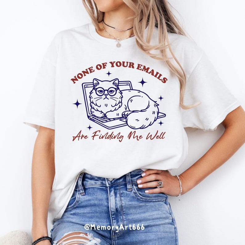 May include: White t-shirt with a blue and white illustration of a cat wearing glasses and sitting on a laptop. The text "NONE OF YOUR EMAILS ARE FINDING ME WELL" is printed in red on the shirt.
