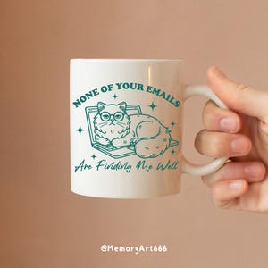 May include: White ceramic mug with a teal outline of a cat wearing glasses and sitting on a laptop. The text on the mug reads "None of your emails are finding me well".