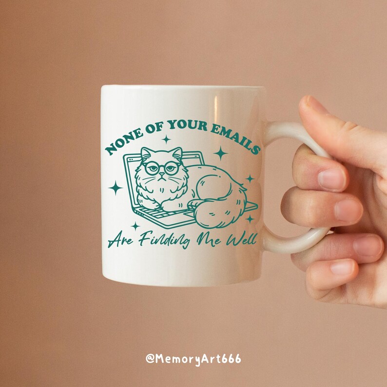 May include: White ceramic mug with a teal outline of a cat wearing glasses and sitting on a laptop. The text on the mug reads "None of your emails are finding me well".