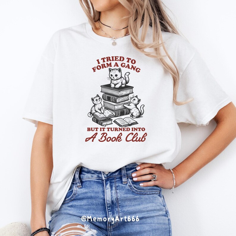 May include: White t-shirt with a graphic of three cats reading books. The text on the shirt reads "I tried to form a gang but it turned into a book club".