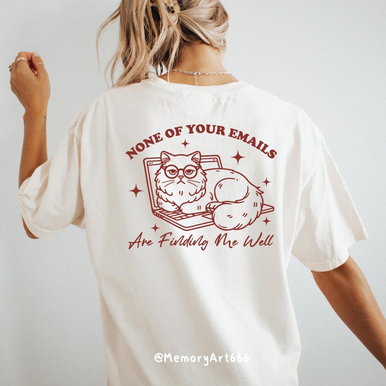May include: White t-shirt with a red graphic of a cat sitting on a laptop. The text on the shirt reads "None of your emails are finding me well."  The text "@MemoryArt666" is at the bottom of the shirt.