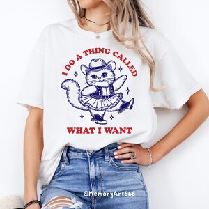 A funny retro-style illustration of a sassy cowboy cat dancing confidently, wearing a western hat, boots, and a skirt. The sarcastic quote reads “I Do A Thing Called What I Want.” Vintage hand-drawn line art with playful details and a bold, confident attitude. Adult humor design with a positive, self-love vibe, perfect for shirts, tote bags, mugs, stickers, and digital crafts. SVG and PNG digital download.