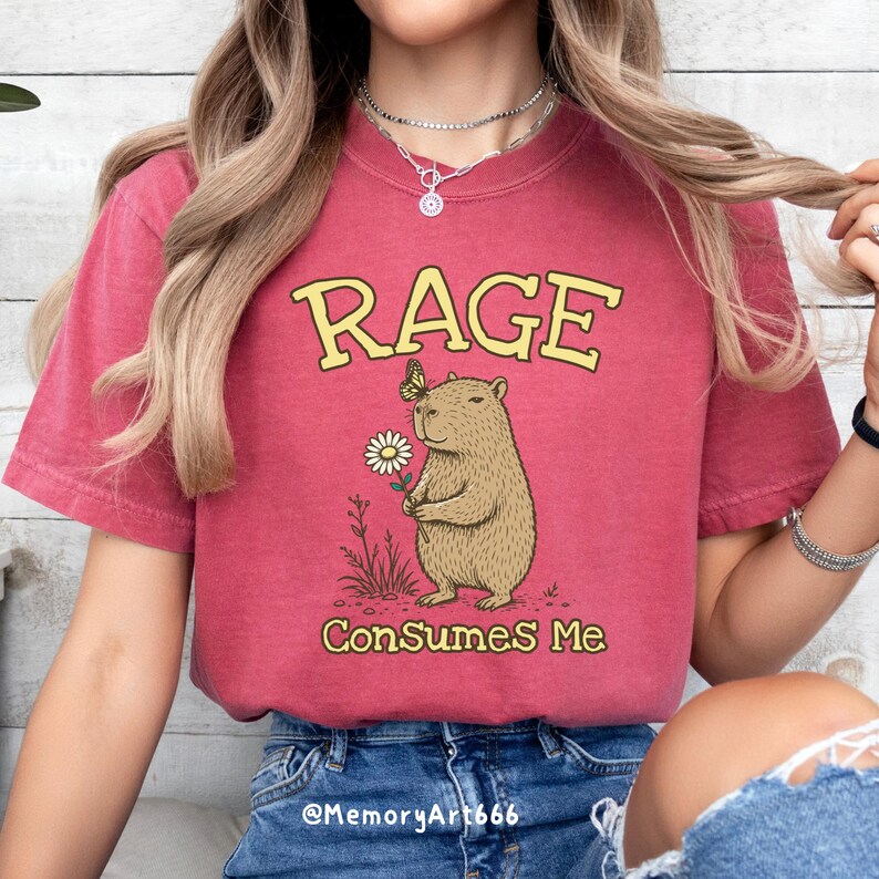 Funny capybara meme PNG SVG design featuring a cute vintage-style capybara holding a daisy flower with a butterfly resting on its head and bold retro “RAGE Consumes Me” typography. Funny sarcastic animal graphic with whimsical hand-drawn line art, soft neutral tones, and trendy unhinged aesthetic. Perfect for funny t-shirts, hoodies, mugs, tote bags, stickers, sublimation projects, Cricut SVG cut files, retro boutique apparel, instant digital download, 300 DPI transparent background.