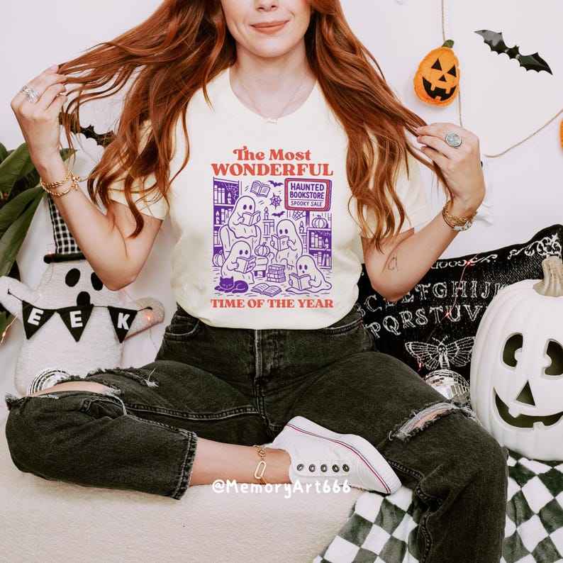 K&ouml;nnte beinhalten: Cremefarbenes T-Shirt mit einem Halloween-Motiv. Das Motiv zeigt Geister, die in einer Buchhandlung lesen, mit dem Text "The Most Wonderful Time of the Year". Das Shirt wird mit schwarzen Jeans und wei&szlig;en Turnschuhen kombiniert.