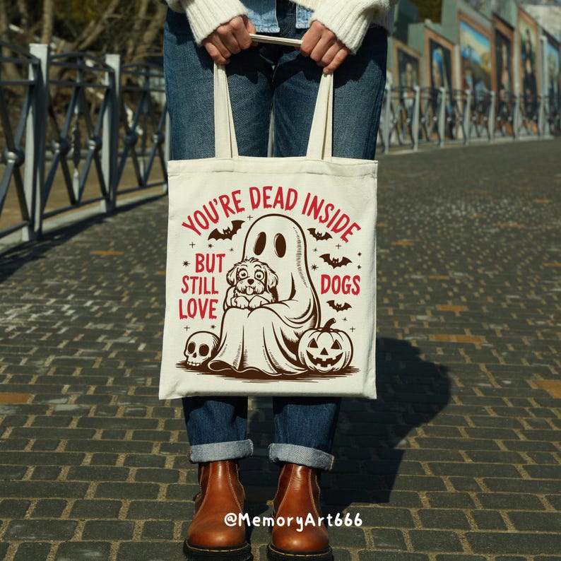 May include: A white tote bag with a ghost and a dog inside. The text on the bag reads "You're Dead Inside But Still Love Dogs".