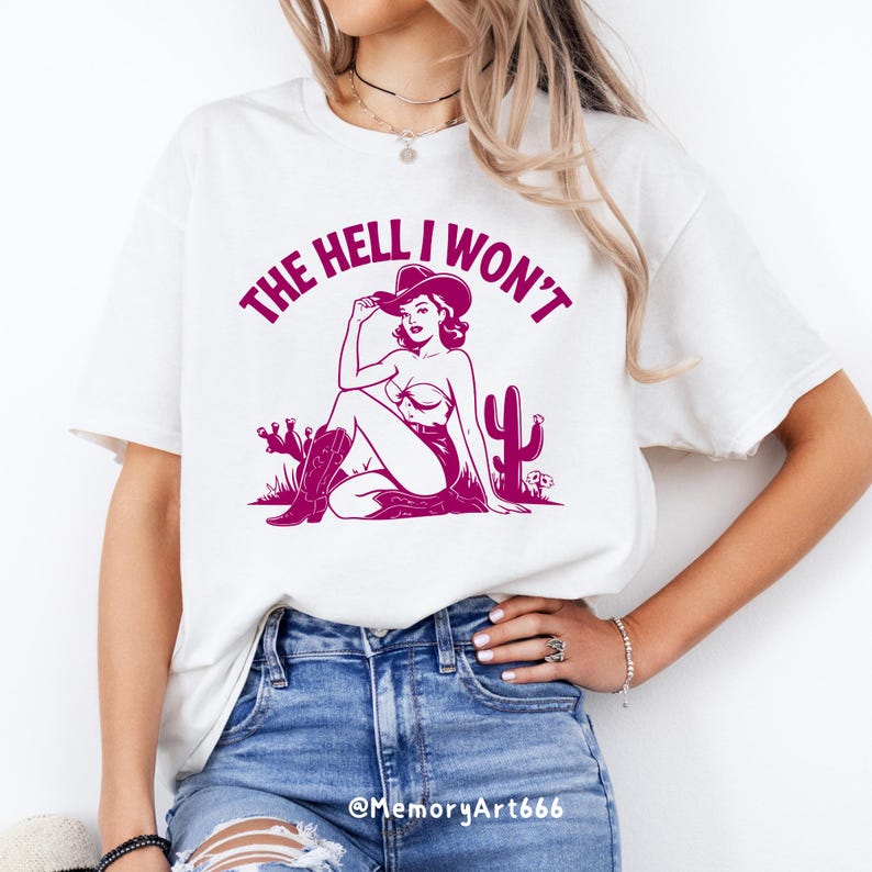 May include: White t-shirt with a pink graphic of a woman wearing a cowboy hat and the text "THE HELL I WON'T".