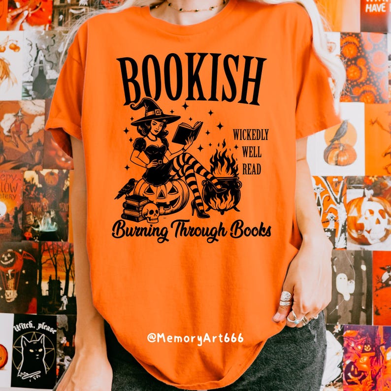 May include: Orange t-shirt with a black graphic featuring a witch reading a book, a cauldron, and the text "BOOKISH" and "Burning Through Books". The witch is sitting on a pumpkin. The shirt has a crew neck.