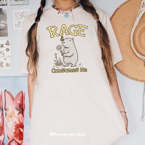 Funny capybara meme PNG SVG design featuring a cute vintage-style capybara holding a daisy flower with a butterfly resting on its head and bold retro “RAGE Consumes Me” typography. Funny sarcastic animal graphic with whimsical hand-drawn line art, soft neutral tones, and trendy unhinged aesthetic. Perfect for funny t-shirts, hoodies, mugs, tote bags, stickers, sublimation projects, Cricut SVG cut files, retro boutique apparel, instant digital download, 300 DPI transparent background.