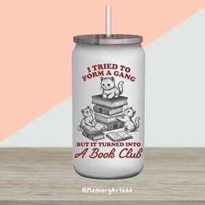May include: White stainless steel tumbler with a wood lid and a straw. The tumbler has a red graphic of three cats reading books with the text "I tried to form a gang but it turned into a book club".