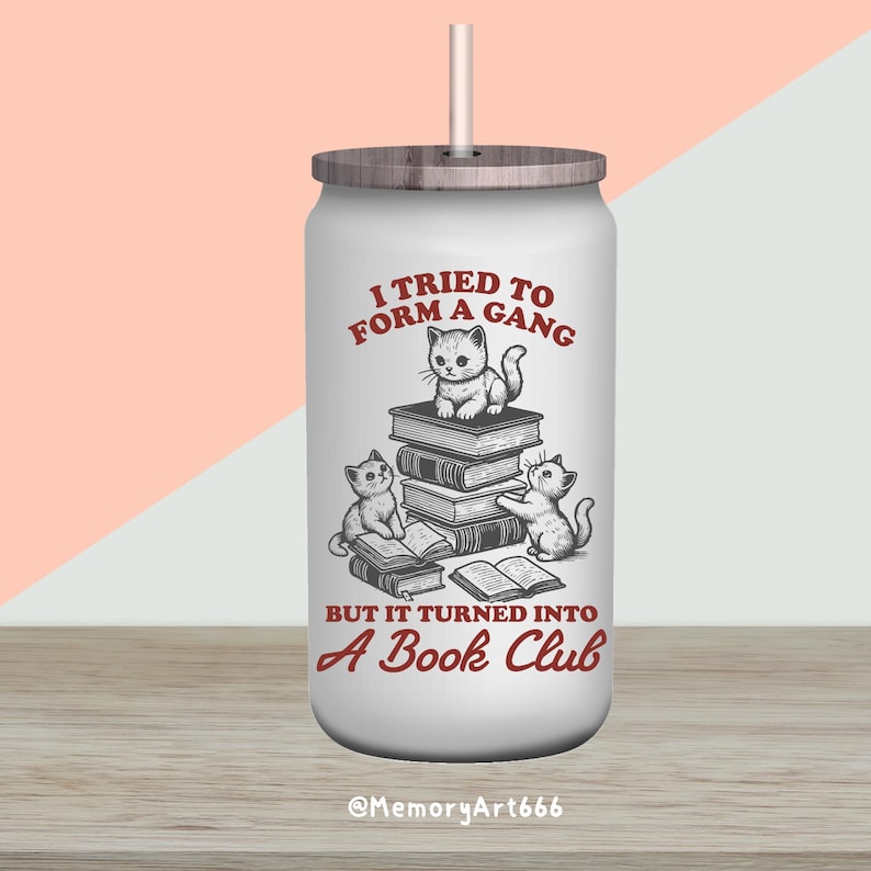 May include: White stainless steel tumbler with a wood lid and a straw. The tumbler has a red graphic of three cats reading books with the text "I tried to form a gang but it turned into a book club".