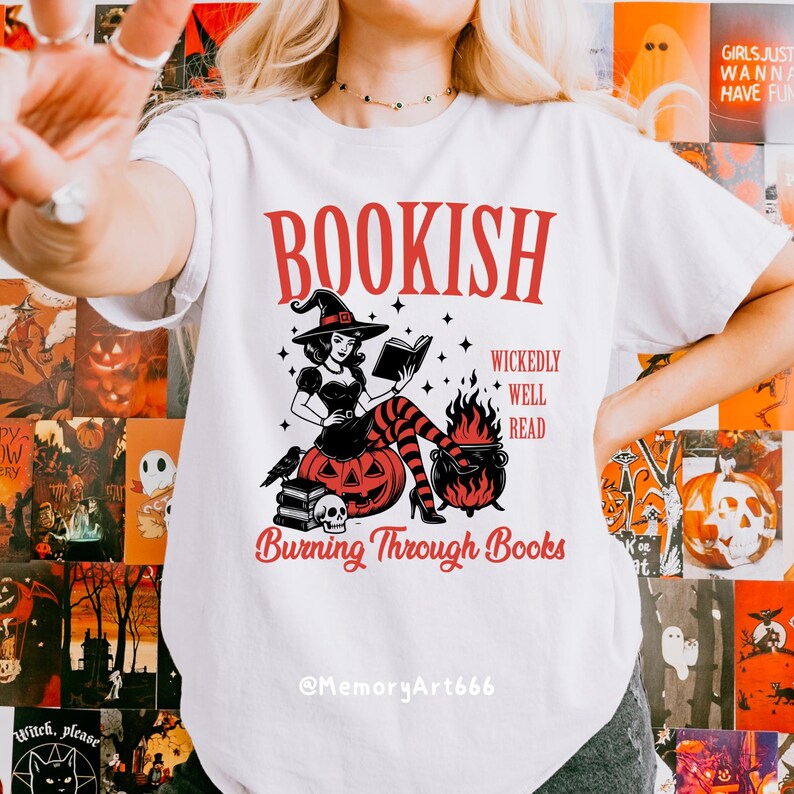 May include: White t-shirt with a red graphic that says "BOOKISH" above an illustration of a witch reading a book. The witch is sitting on a pumpkin with a skull and books. The text "Burning Through Books" is below the illustration.