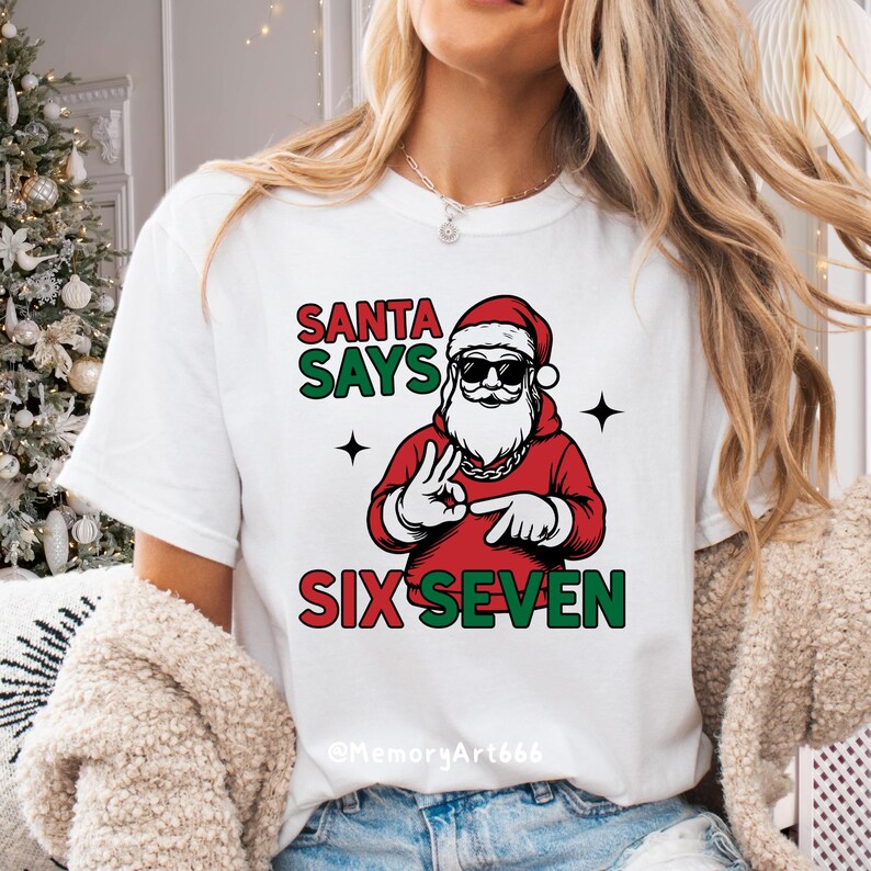 May include: White t-shirt with a graphic of Santa Claus wearing sunglasses and a red hoodie. The text "SANTA SAYS SIX SEVEN" is printed above and below the Santa graphic in green and red.