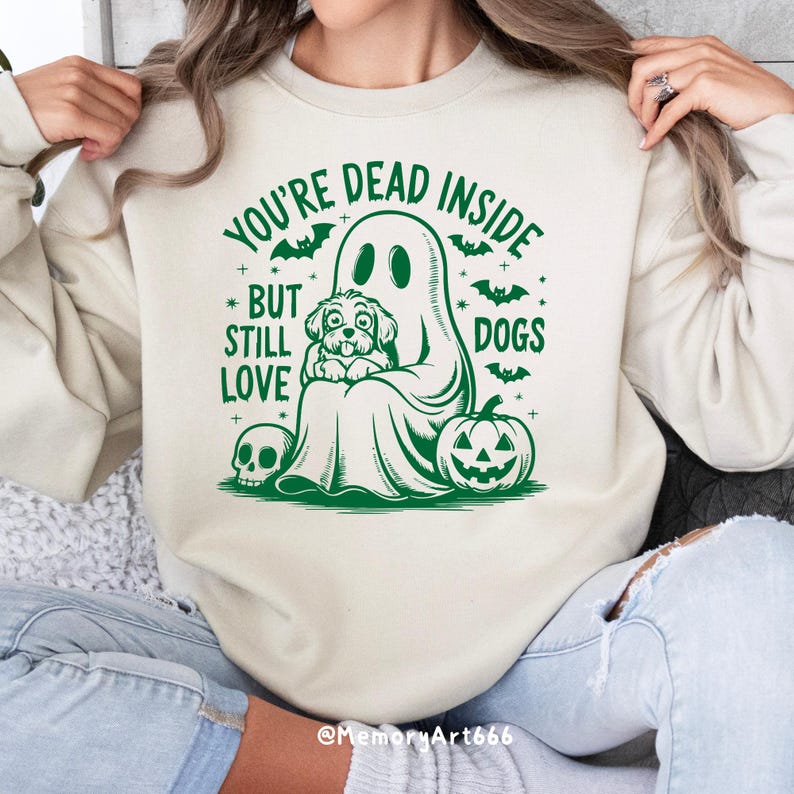 May include: A cream-colored sweatshirt with a green graphic of a ghost holding a dog. The text on the sweatshirt reads "You're Dead Inside But Still Love Dogs".