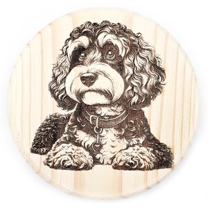 May include: A black and white woodburned image of a dog with curly hair, wearing a collar with a heart charm. The image is on a round wooden plaque.