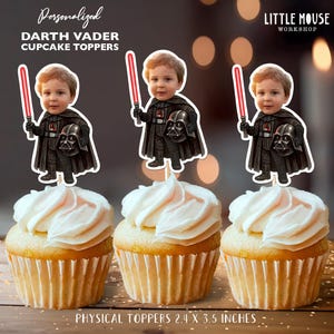 Może przedstawiać: Trzy babeczki z białym lukrem, każda ozdobiona spersonalizowaną nakładką na babeczkę Darth Vader. Nakładki przedstawiają dziecko przebrane za Dartha Vadera, trzymające czerwony miecz świetlny. Nakładki mierzą 6,1 x 8,9 cm.