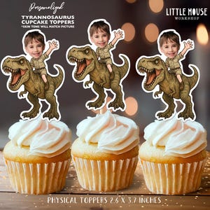 May include: Three cupcakes with white frosting and Tyrannosaurus cupcake toppers. The toppers show a child riding a dinosaur. The text on the toppers reads "Personalized Tyrannosaurus Cupcake Toppers". The physical toppers are 6.6 x 9.4 cm.