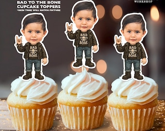 May include: Three cupcakes topped with personalized "Bad to the Bone" toppers. Each topper features a cartoon figure in a leather jacket and jeans. The cupcakes have white frosting. The text "Personalized Bad to the Bone Cupcake Toppers" is at the top.