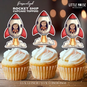 Op de afbeelding: Drie cupcake-toppers met een cartoon-raket met een kindergezicht in het raam. De raket is rood, wit en geel met een rookwolk erachter. De toppers zijn 2,5 inch bij 3,8 inch en zijn geprint op 8,5 inch bij 11 inch papier.