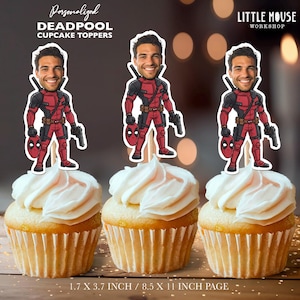Puede incluir: Tres cupcakes con glaseado blanco, cubiertos con adornos para cupcakes de Deadpool. Los adornos presentan una ilustraci&oacute;n de dibujos animados de Deadpool sosteniendo un arma y su m&aacute;scara. El texto en la imagen dice: "Personalized DEADPOOL CUPCAKE TOPPERS" y "LITTLE MOUSE WORKSHOP".