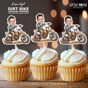 Puede incluir: Tres cupcakes cubiertos con glaseado blanco, cada uno con un adorno personalizado para cupcakes de motocross. Los adornos presentan a un niño de dibujos animados en una moto de cross amarilla y marrón. El texto en los adornos dice "Personalized DIRT BIKE CUPCAKE TOPPERS".