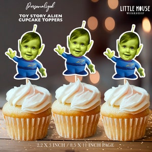 May include: Three green alien cupcake toppers with blue outfits and a space logo. The aliens have human faces and are personalized with photos. The toppers are 2.2 inches by 3 inches and are printed on an 8.5 inch by 11 inch page.