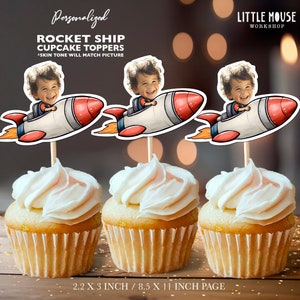 May include: Three personalized rocket ship cupcake toppers with a child's face in the cockpit. The toppers are 2.2 inches by 3 inches and are printed on 8.5 inch by 11 inch paper.  The text "Personalized Rocket Ship Cupcake Toppers" and "Skin tone will match picture" is printed at the top of the image. The text "Little Mouse Workshop" is printed in the upper right corner of the image.